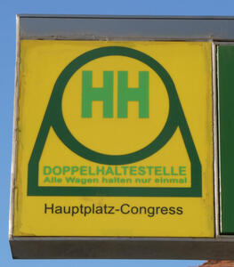 Sign with two green letter H in green circle on yellow background. Doppelhaltestelle / Alle Wagen halten nur einmal