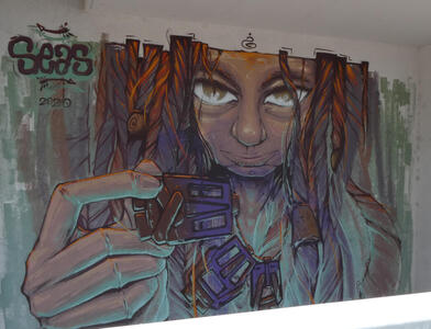 Person with long hair,staring at viwer and holding a necklace toward the viewer