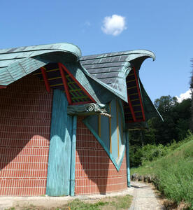 Back side of church. Roof is shaped like wings, and there is a bird’s head and neck projecting from the wall.