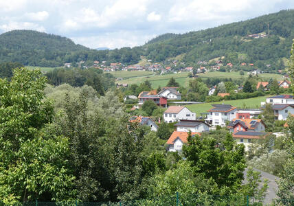 In foreground, trees. In background, rolling hills with houses on them.