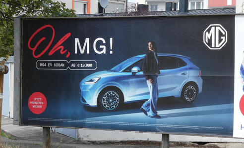 Woman standing near a blue MG car. Text: Oh, MG!