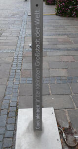 Vertical columnar drinking fountain. Text: Cool bleiben in der kleinsten Großstadt der Welt.