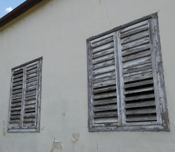 Old rickety shutters wih peeling white paint and gray wood beneath.