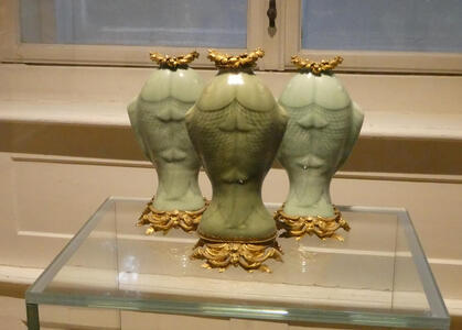 Three light-green fish-shaped urns. They are standing on their tail, and the base of each is gold.