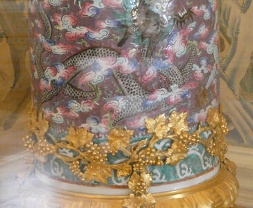 Base of a column decorated with gold grape vine. The column has an oriental-style snake cured around it.