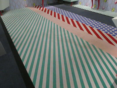 Carpet with green stripes, a tan area, red stripes, and a blue polka-dotted section
