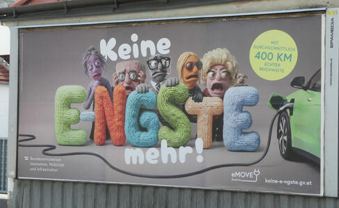 Crocheted people looking anxiously at an electric car being charged. They are behind crocheted letters. Text: Keine E-NGSTE mehr! mit durchschnittlich 400 KM echter reichweite