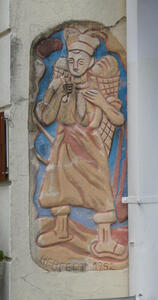 Painted carving on wall, depicting a man carrying loaves of bread in bags on his back.
