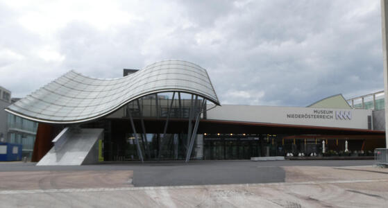 Building with tilted, sinusoidal roof area. At right, the name of the museum