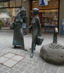Life-size metal sculpture of two women carrying shopping bags and having a conversation