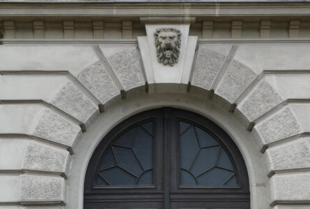 Arch above doorway. In middle of arch, a sculpture of a lion’s head