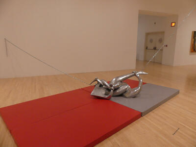 Abstract metal sculpture of intertwined arms, chained to walls, resting on red and gray exercise mats