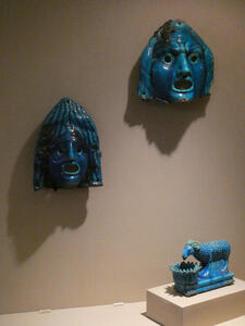 Two blue ceramic masks and sculpture of sheep drinking water