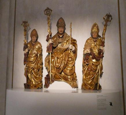 Wooden statues of three archbishops holding staffs and wearing miters. They all seem to have shocked expressions.