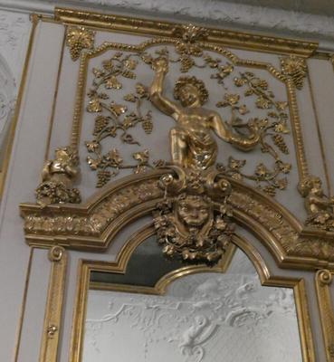 Gold decoration above a mirror. Depicts a youth with hand upraised.