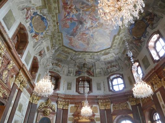 Ceiling of a large room. The ceiling is painted with a fresco, and there are several crystal chandeliers.
