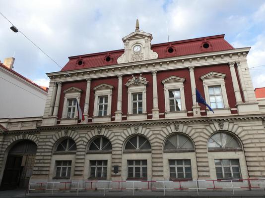 Government building with red facade on top floor. Czech flag at left, EU flag at right