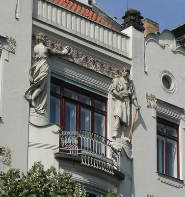 Balcony with wrought iron fencing; to left, statue of woman. To right, a man with a gold sword
