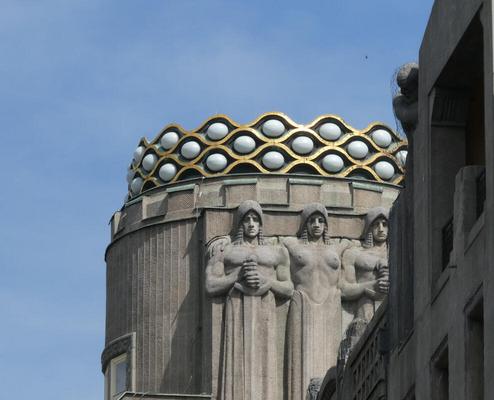 Cylindrical column. At top, a “necklace” of beads framed in gold. Beneath, statues of men with swords.