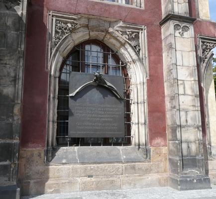 Large metal plaque in arched window. Plaque has what looks like metal-sculpted flowing banner on it