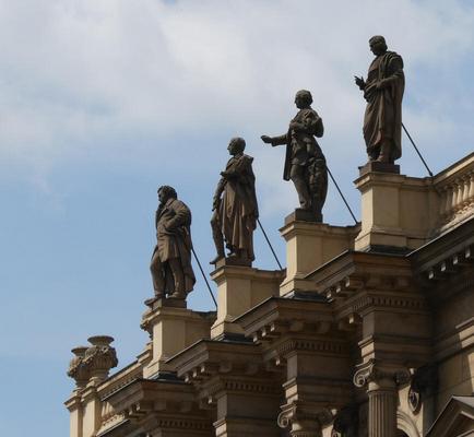 side view of four statues atop a buiding. You can see the supporting rods behind them.