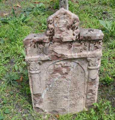Badly weathered headstone with house-shaped section at top