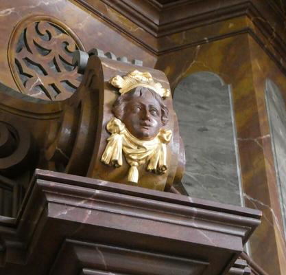 Carved head of child atop a column. The carving is surrounded by gold decoration