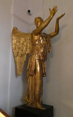 Gold statue of angel holding its hands upraised, palms up.