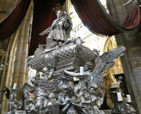 Silver burial casket; atop it, a man holding a cross.