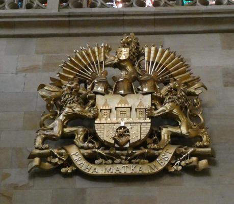 Gold coat of arms with three lions, two at right and left, one at top. in center, three towers above a wall.
