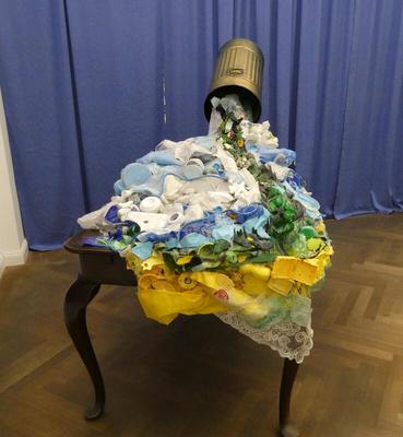 Garbage can titled above a table; on table, cups, saucers, plants.