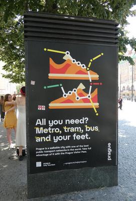 Poster for prague with subway diagram for shoelaces on a pair of shoes. Text: All you need? Metro, tram, bus, and your feet. Someone has put yellow tape across metro, tram, bus, and the word “and”.
